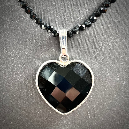 A silver heart shape black stone necklace.  The heart is a faceted cut black spinel, and the pendant is on faceted black spinel beads.