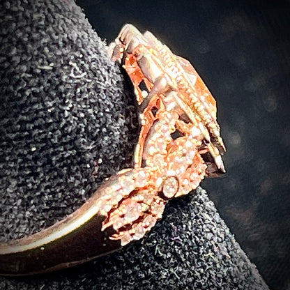 A rose gold plated ring set with a cushion cut morganite stone surrounded by cubic zirconia halos.