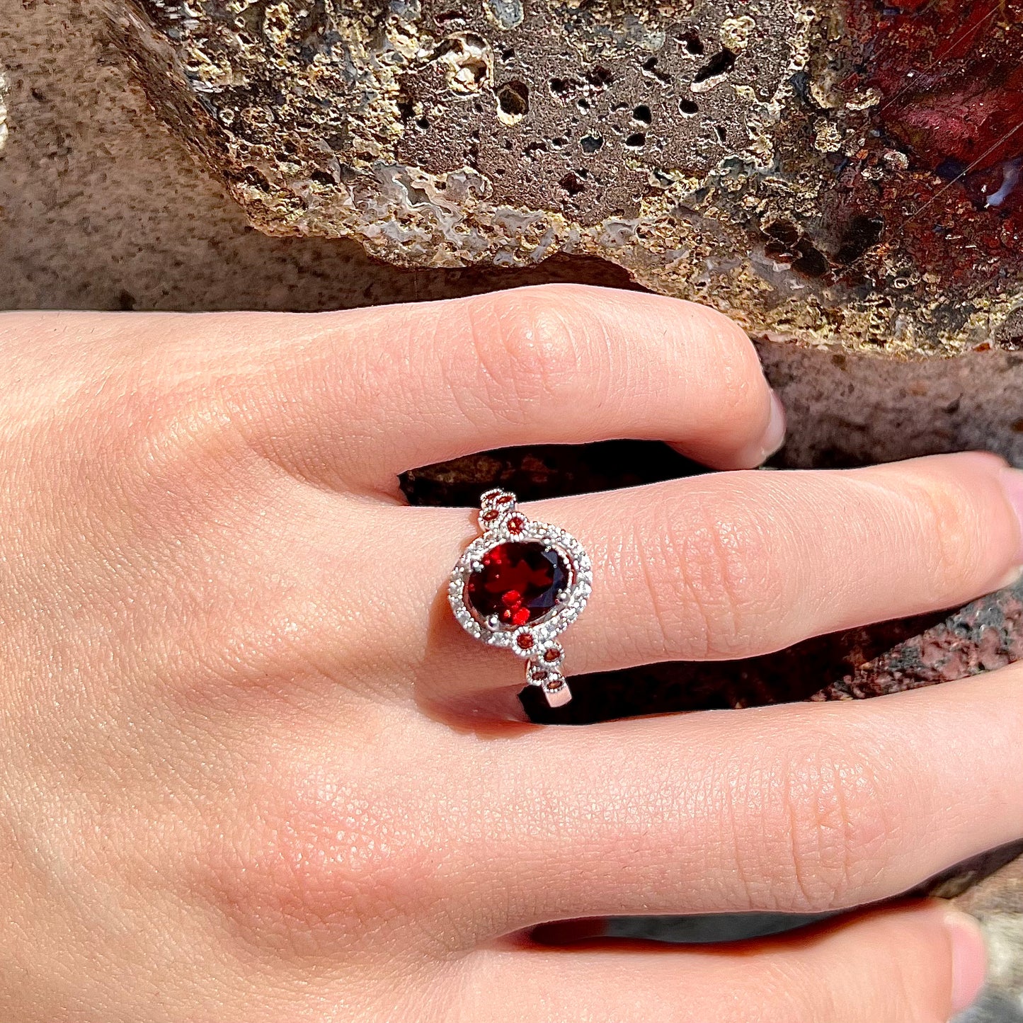 A silver garnet and CZ halo ring.  The center stone is a red almandine garnet, and the side garnets are orange.