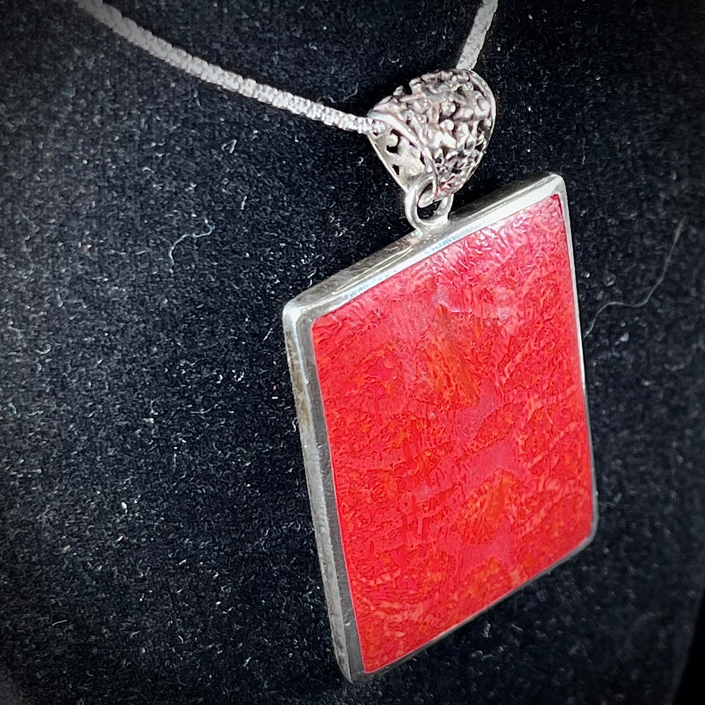 A sterling silver pendant set with rectangular slices of abalone shell and red fossil coral.