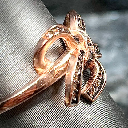 A rose gold colored bow ring.  The bow is tied in a knot, and the knot is set with cognac cubic zirconia.