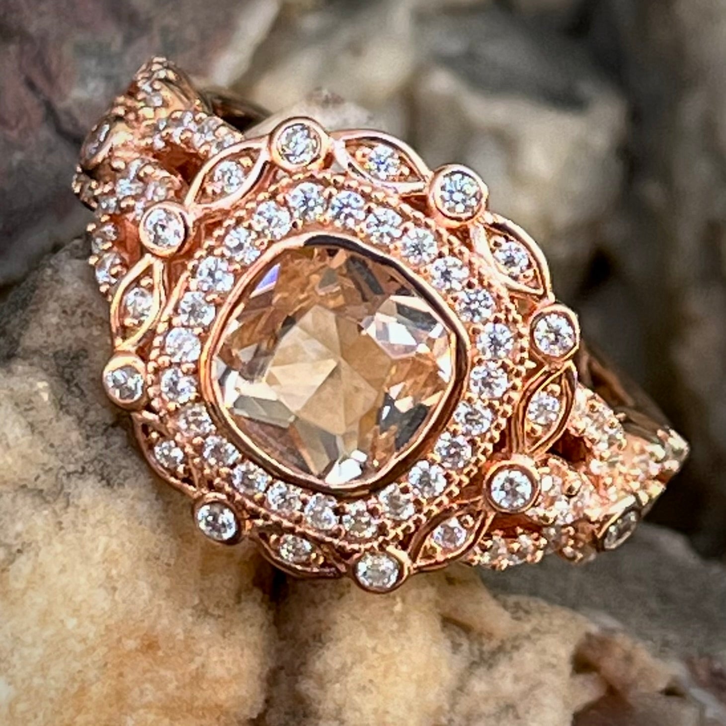 A rose gold plated ring set with a cushion cut morganite stone surrounded by cubic zirconia halos.