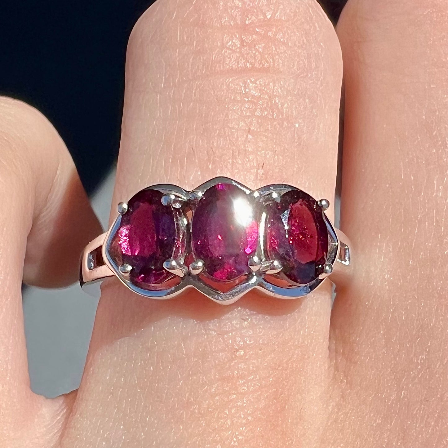 A three stone past, present, and future purple faceted oval cut rhodolite garnet ring.