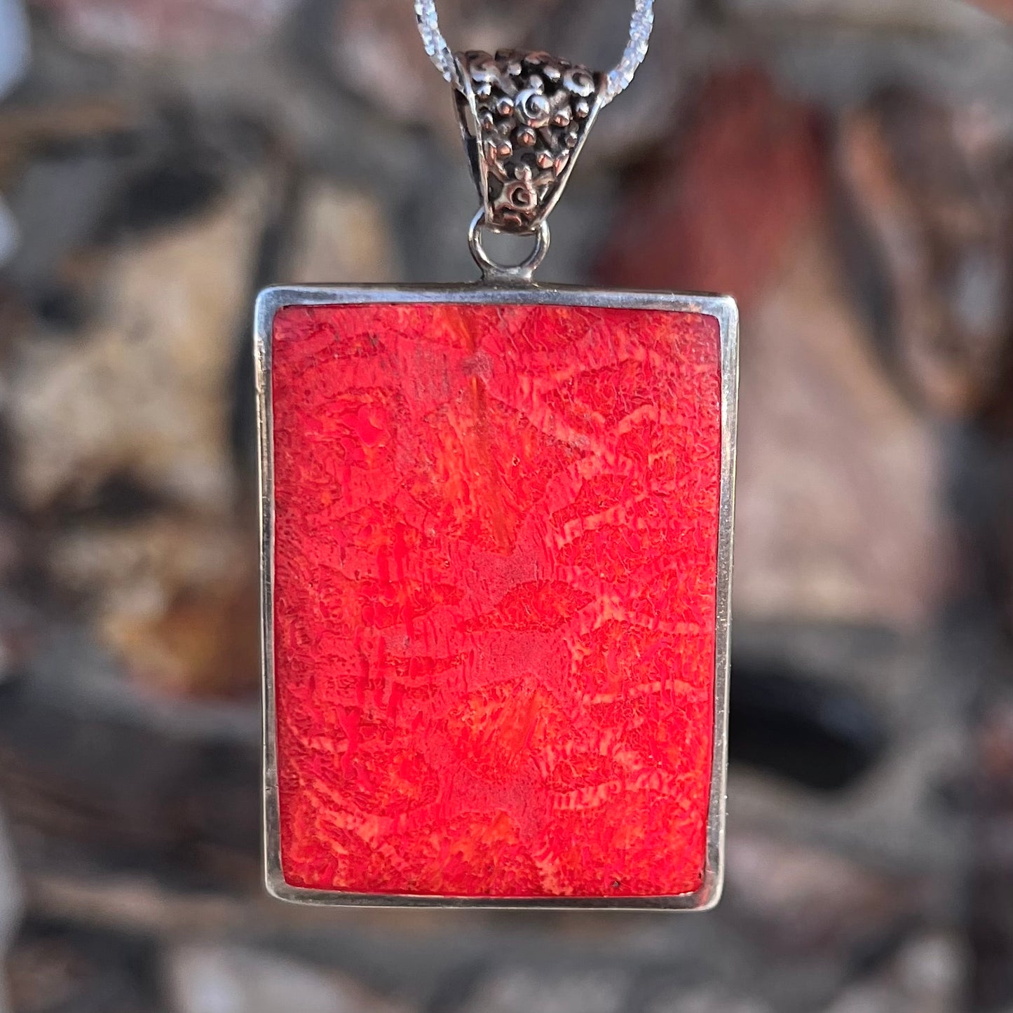 A sterling silver pendant set with rectangular slices of abalone shell and red fossil coral.