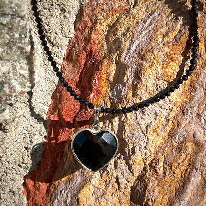 A silver heart shape black stone necklace.  The heart is a faceted cut black spinel, and the pendant is on faceted black spinel beads.