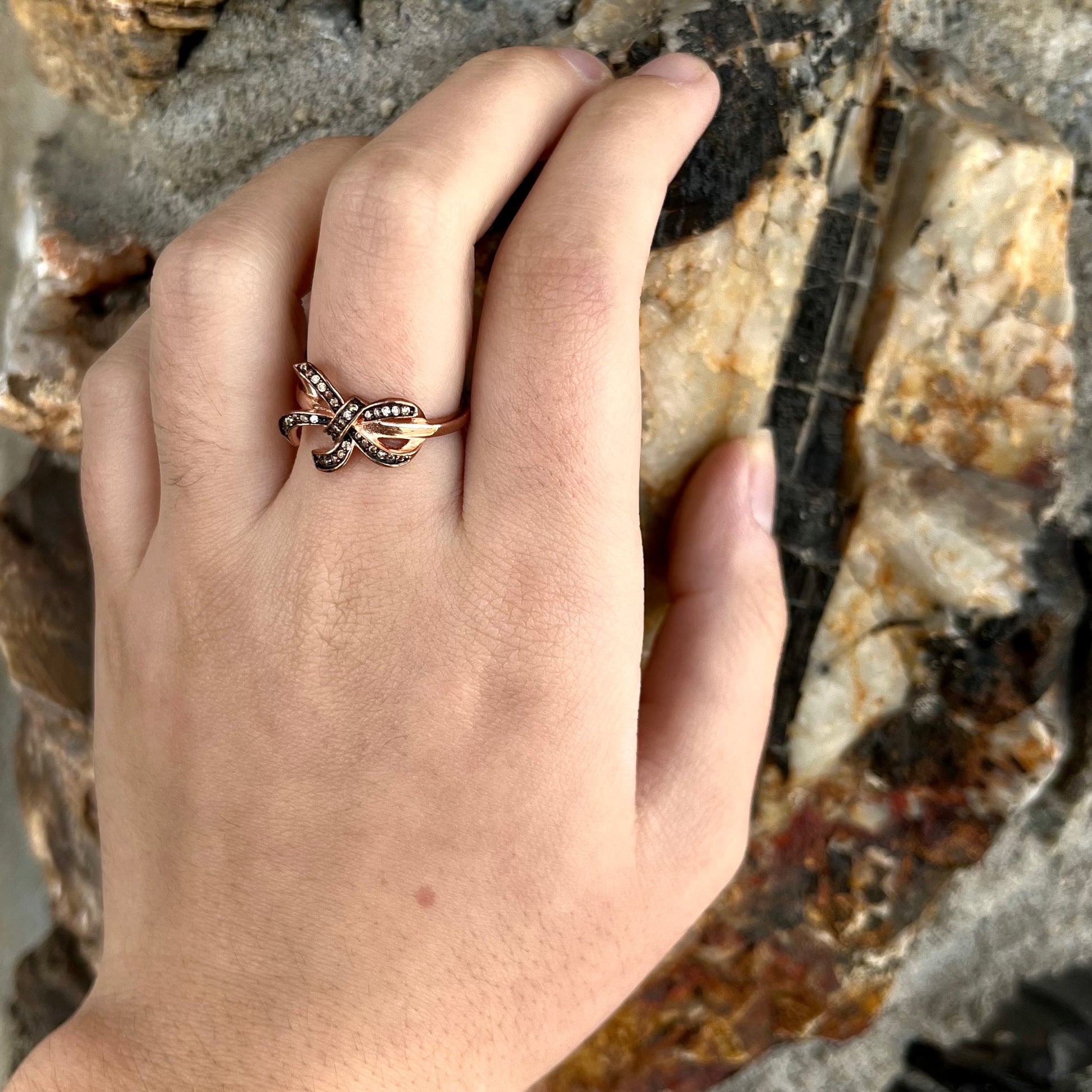 A rose gold colored bow ring.  The bow is tied in a knot, and the knot is set with cognac cubic zirconia.