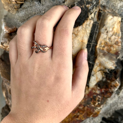 A rose gold colored bow ring.  The bow is tied in a knot, and the knot is set with cognac cubic zirconia.