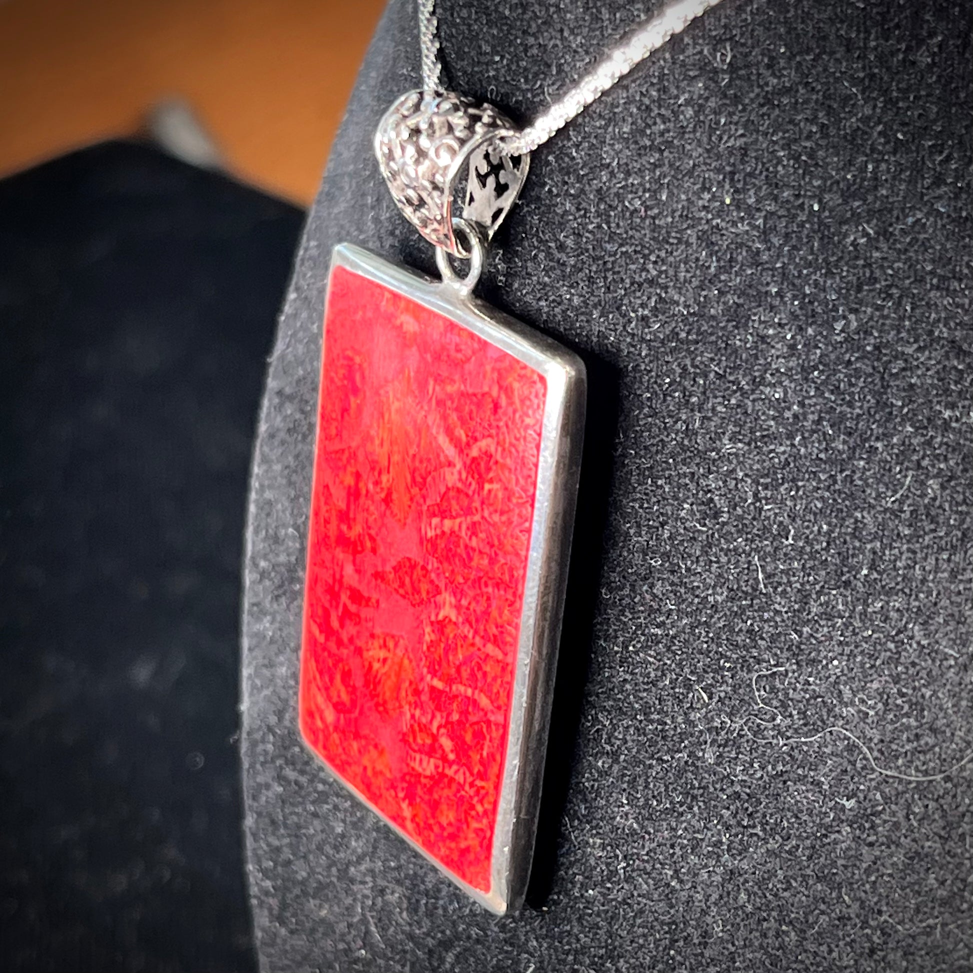 A sterling silver pendant set with rectangular slices of abalone shell and red fossil coral.