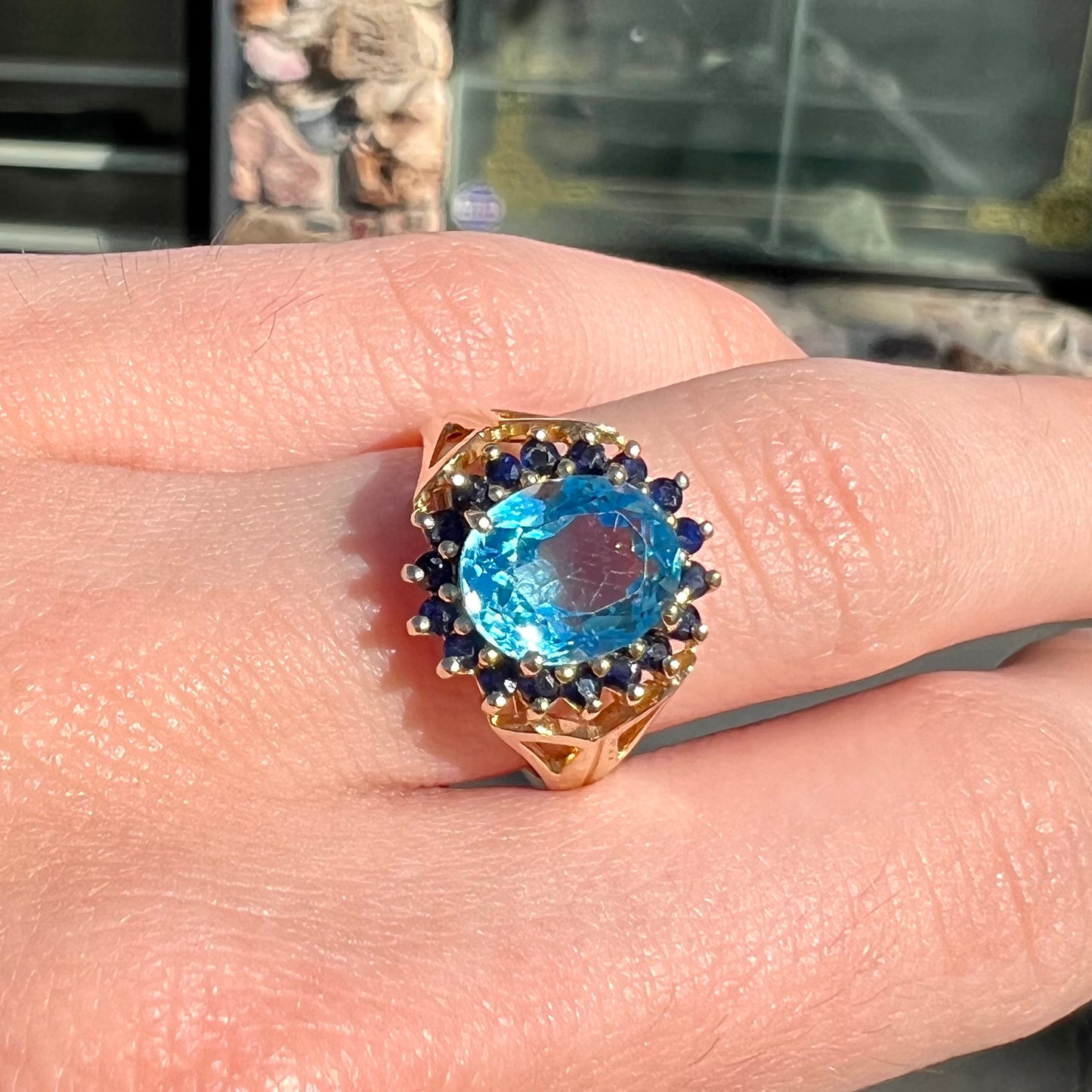 Yellow gold ring prong set with swiss blue topaz center stone and a halo of blue round blue sapphires.