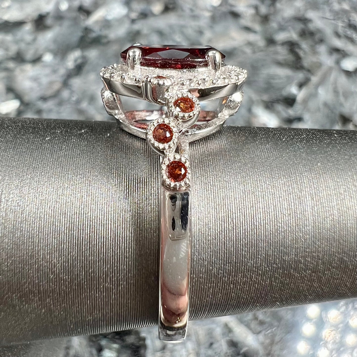 A silver garnet and CZ halo ring.  The center stone is a red almandine garnet, and the side garnets are orange.