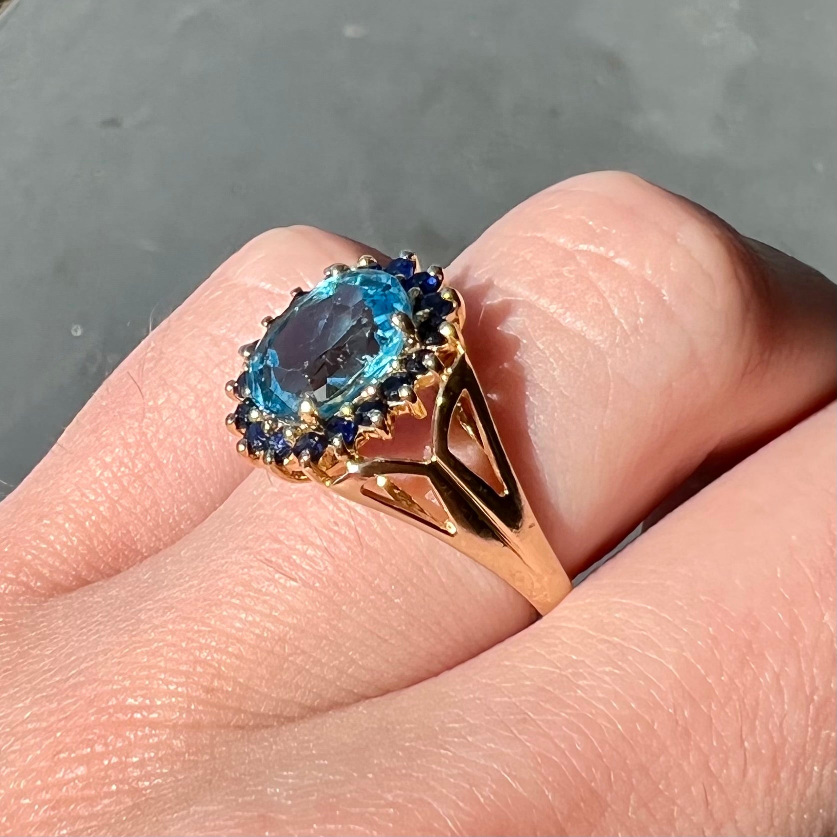 Yellow gold ring prong set with swiss blue topaz center stone and a halo of blue round blue sapphires.