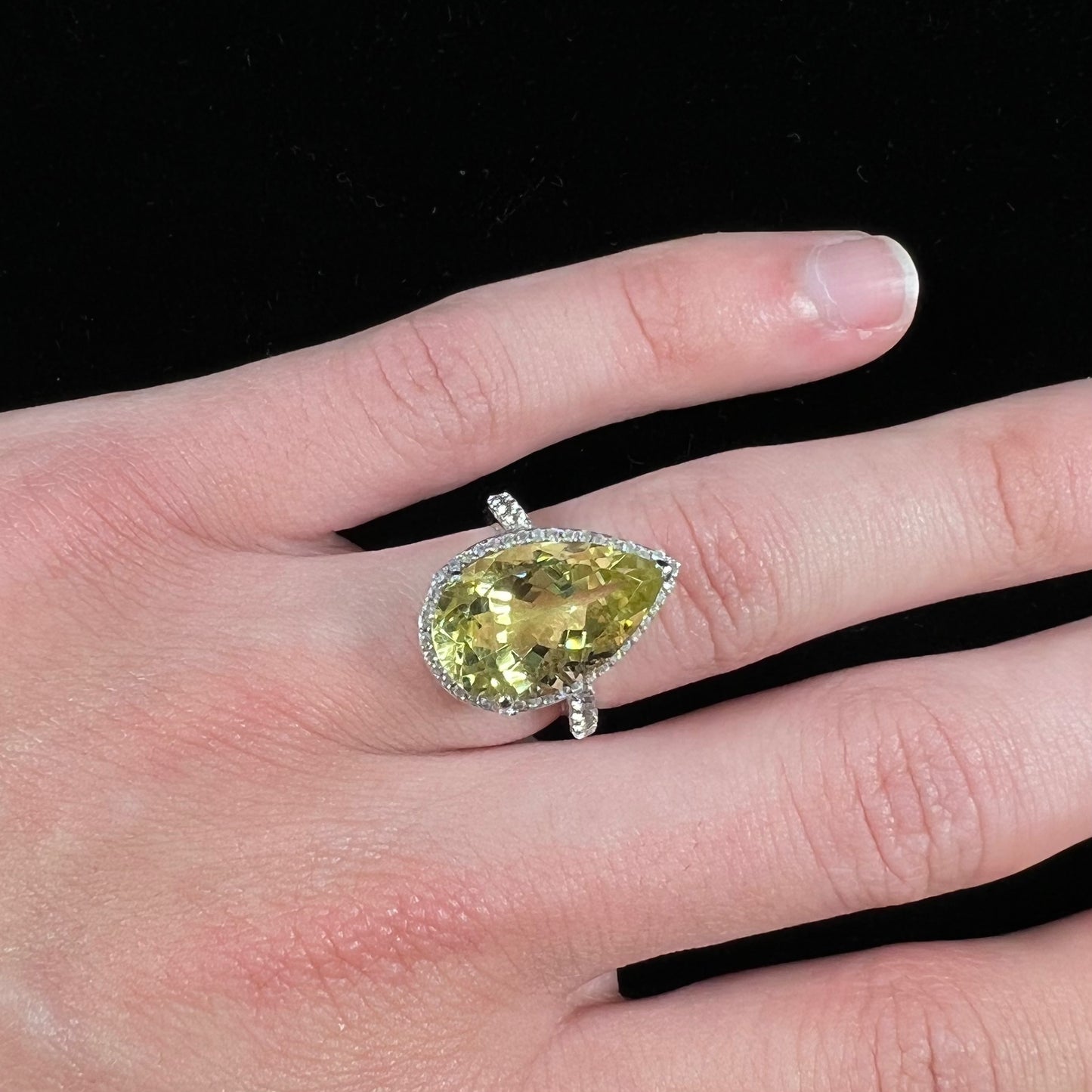 A pear shape lemon quartz set in a sterling silver and white topaz halo ring.