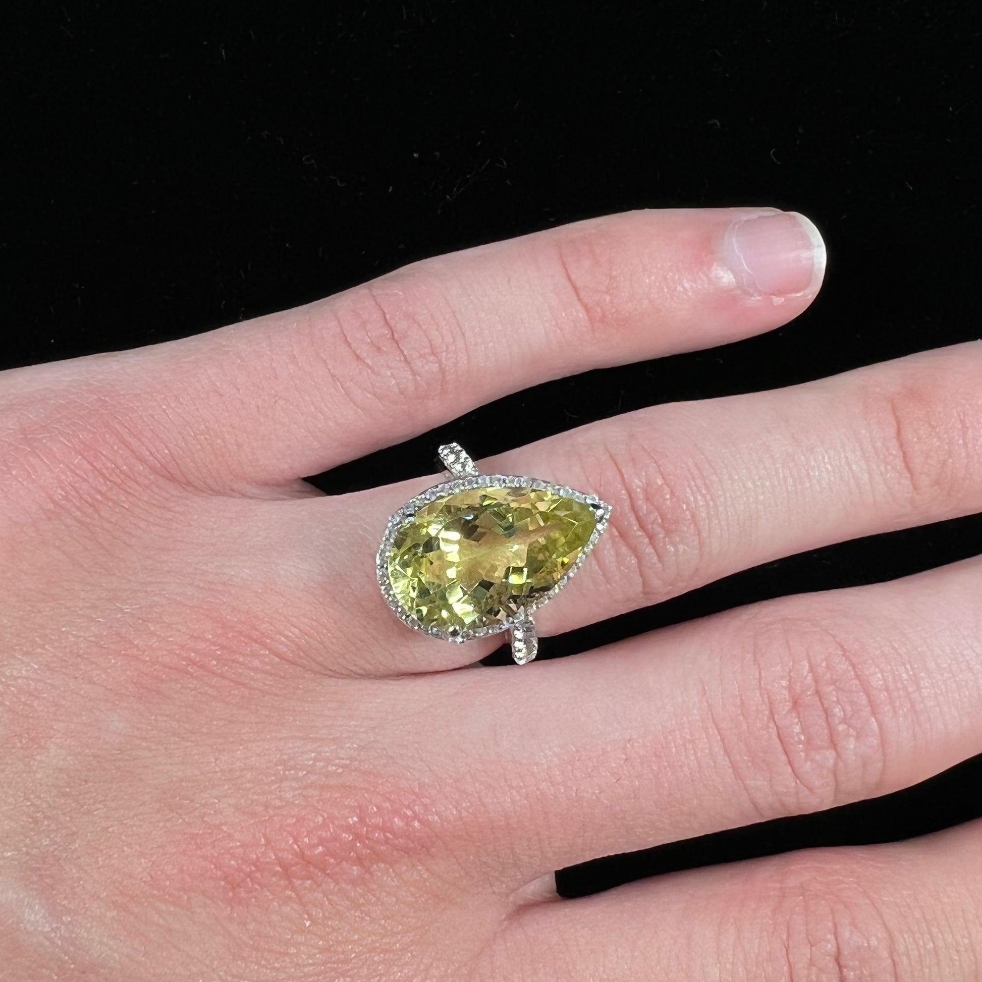 A pear shape lemon quartz set in a sterling silver and white topaz halo ring.
