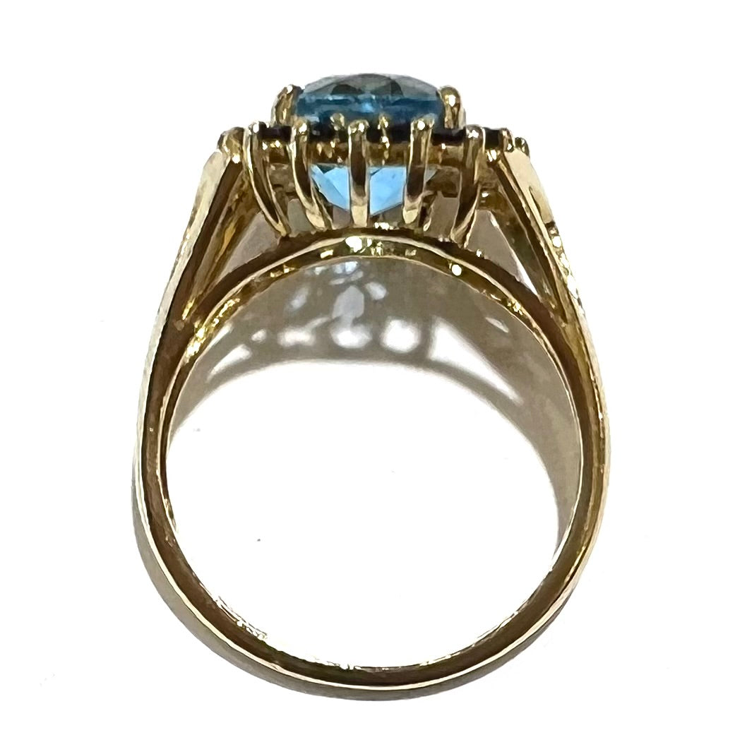 Yellow gold ring prong set with swiss blue topaz center stone and a halo of blue round blue sapphires.