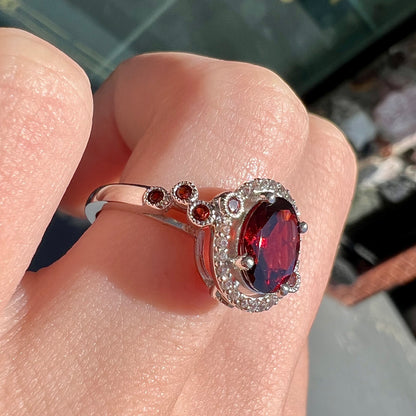 A silver garnet and CZ halo ring.  The center stone is a red almandine garnet, and the side garnets are orange.