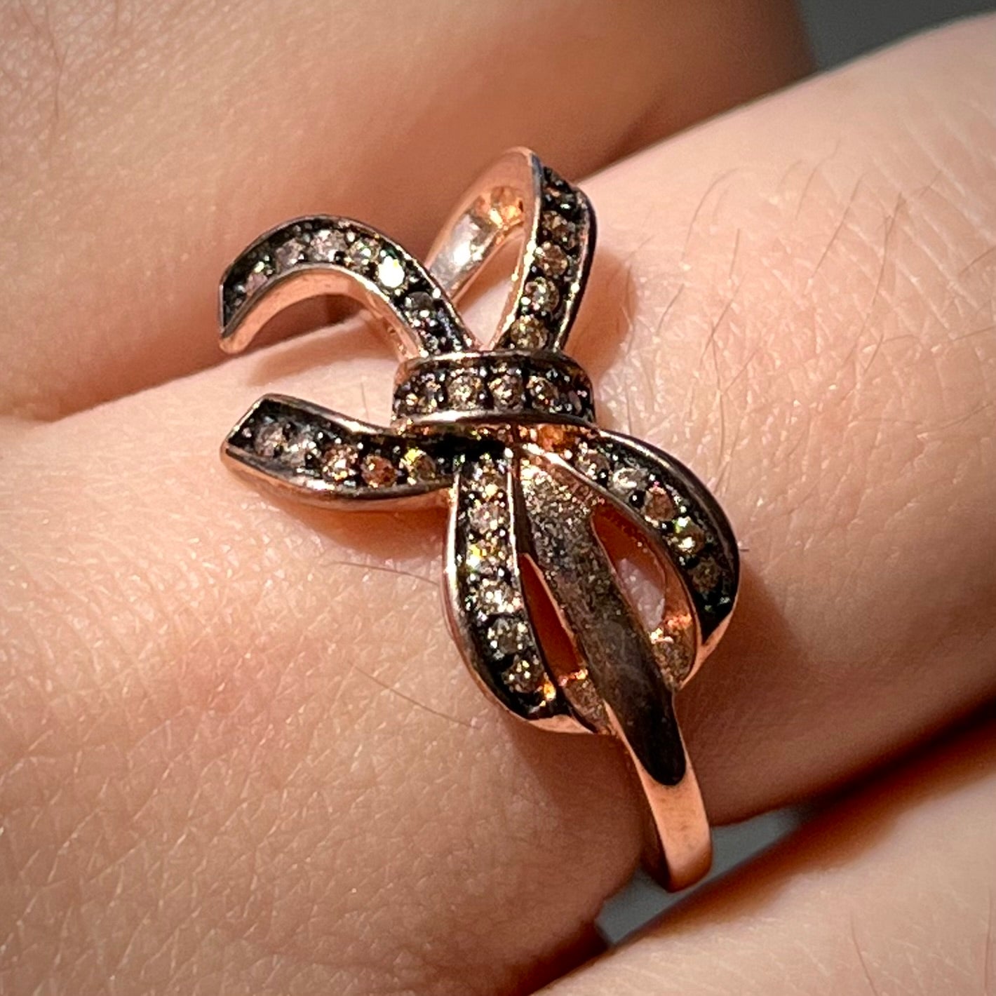 A rose gold colored bow ring.  The bow is tied in a knot, and the knot is set with cognac cubic zirconia.