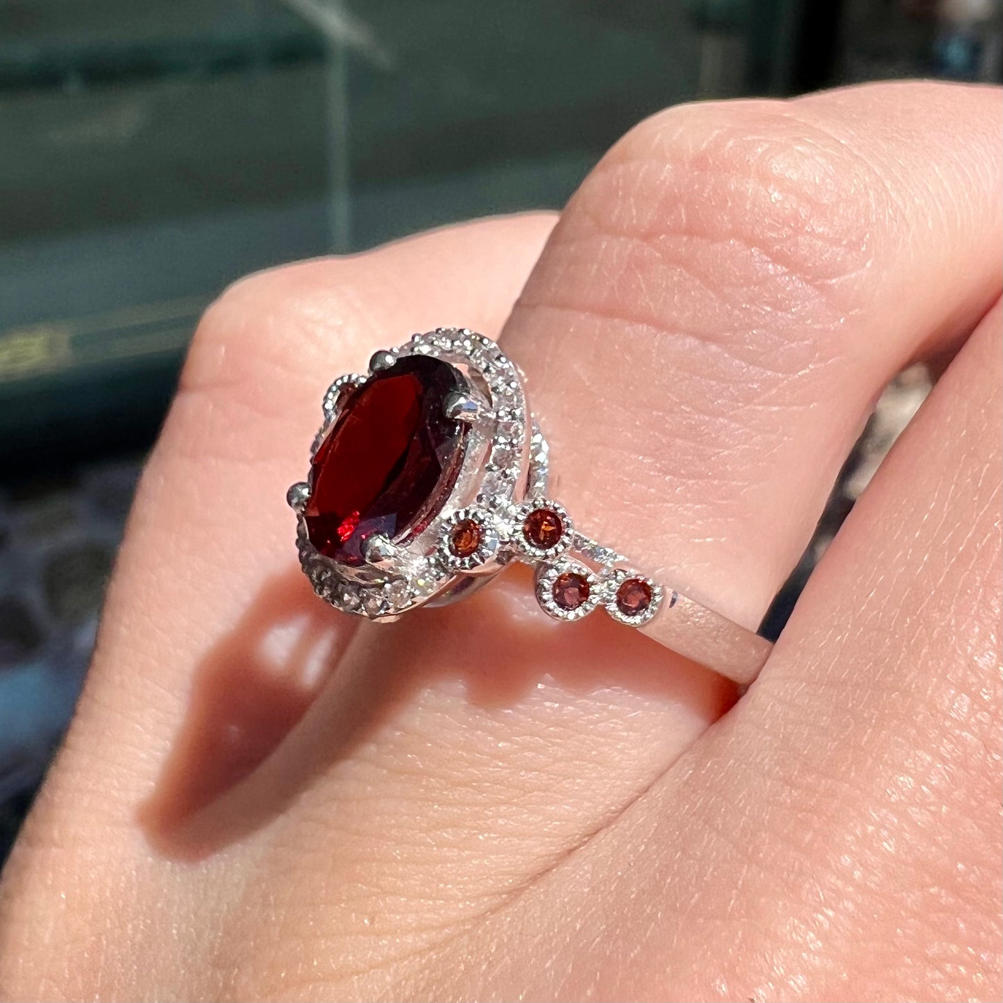 A silver garnet and CZ halo ring.  The center stone is a red almandine garnet, and the side garnets are orange.