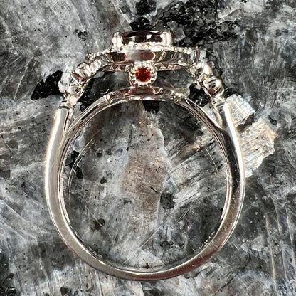 A silver garnet and CZ halo ring.  The center stone is a red almandine garnet, and the side garnets are orange.