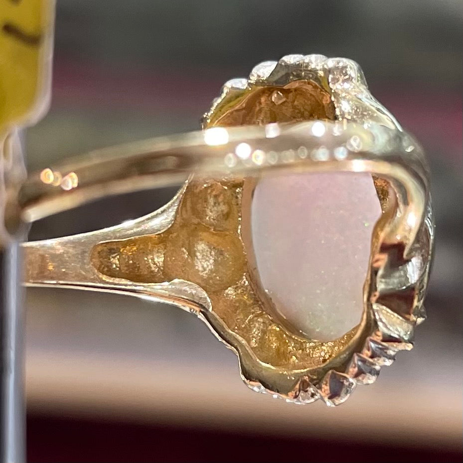 A yellow gold ring set with a synthetic, lab created white opal and two natural diamond accents.