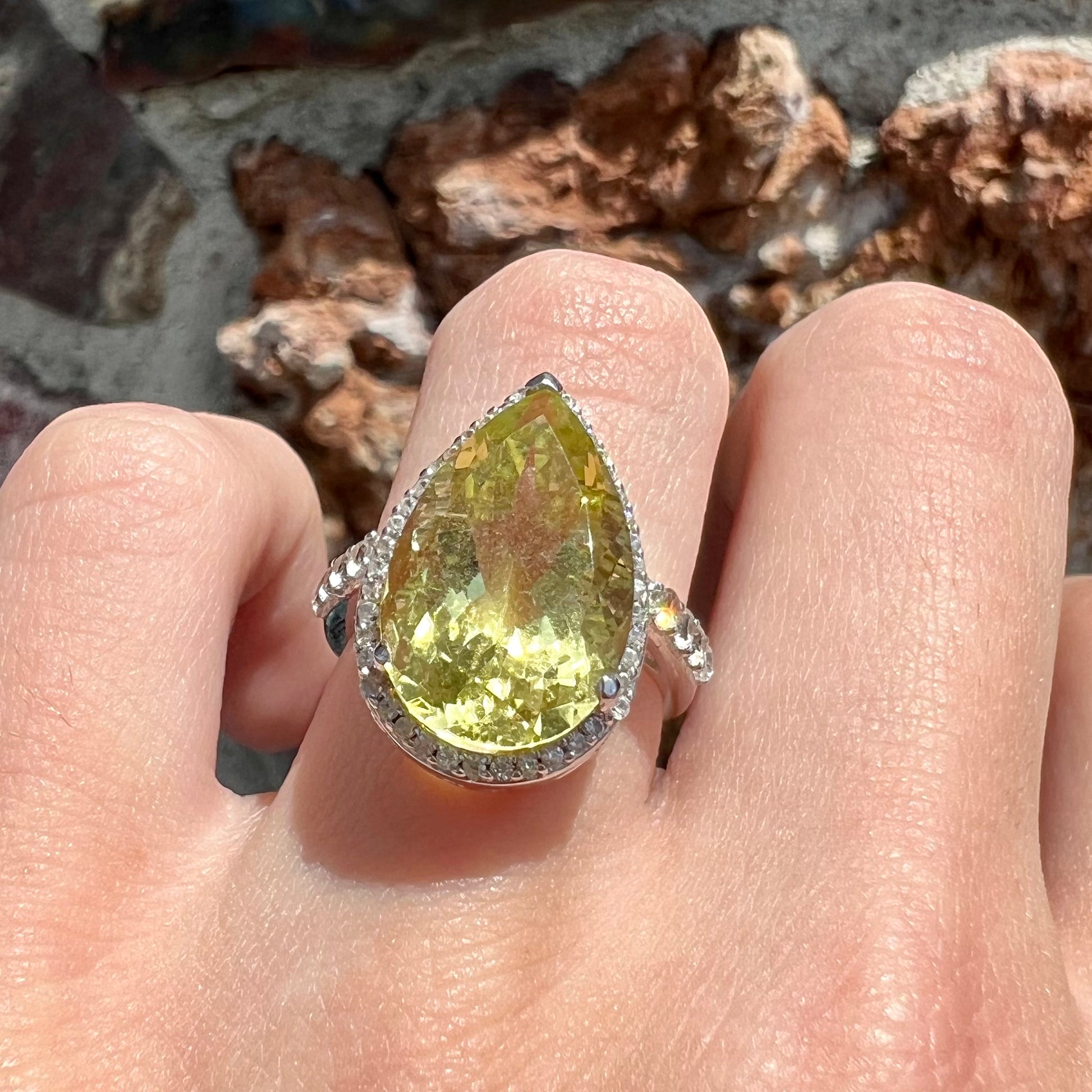 A pear shape lemon quartz set in a sterling silver and white topaz halo ring.