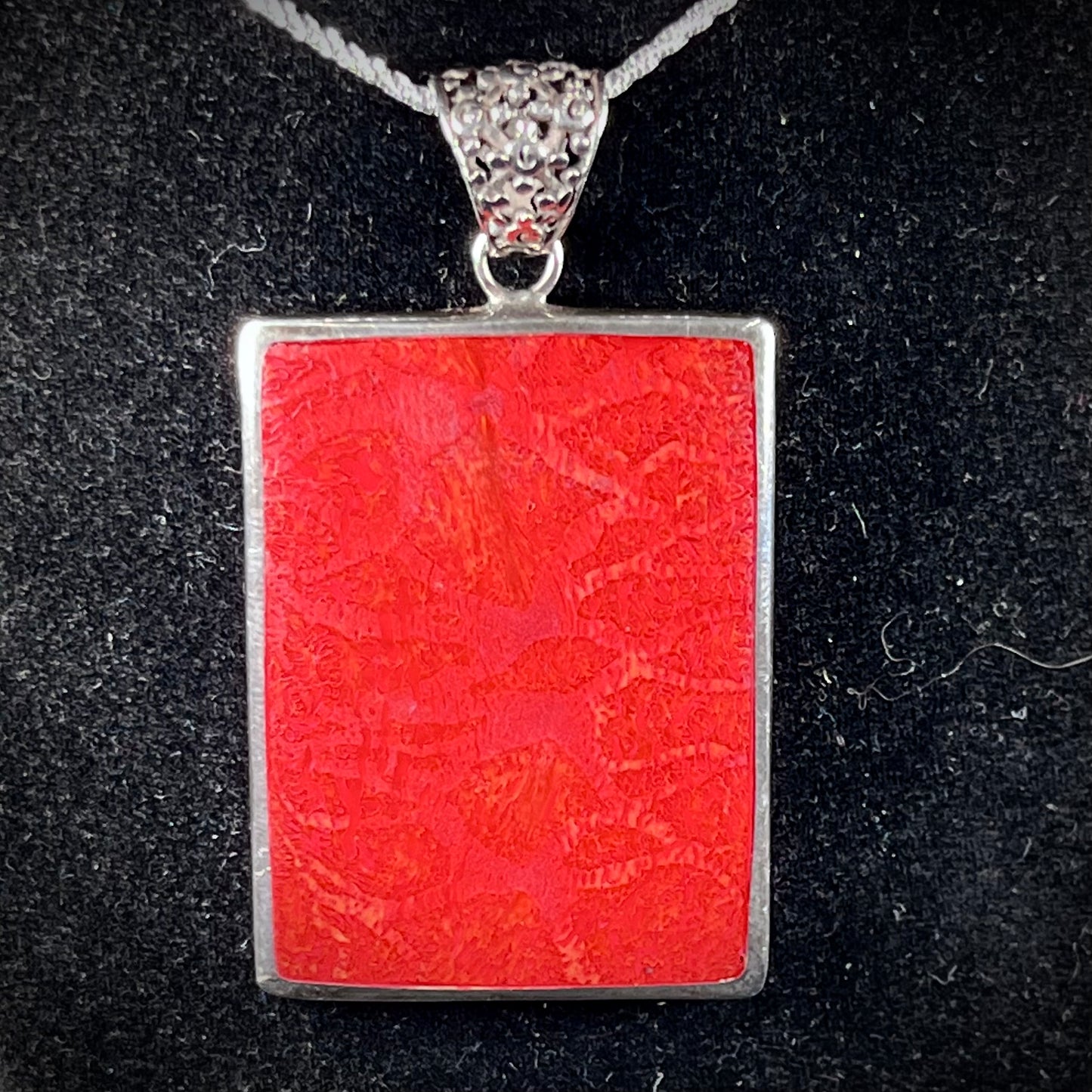 A sterling silver pendant set with rectangular slices of abalone shell and red fossil coral.