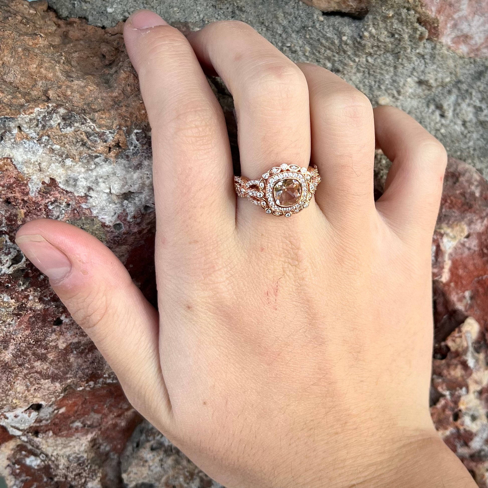 A rose gold plated ring set with a cushion cut morganite stone surrounded by cubic zirconia halos.