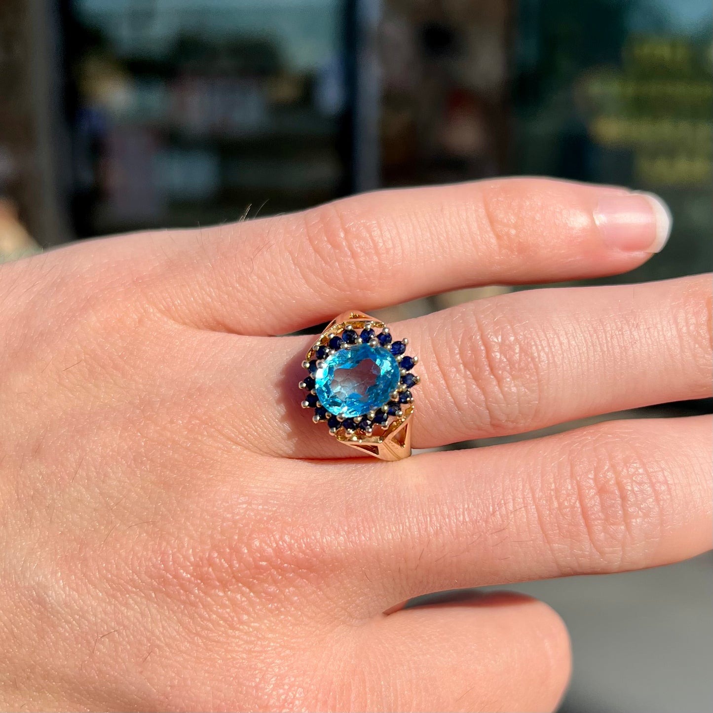 Yellow gold ring prong set with swiss blue topaz center stone and a halo of blue round blue sapphires.