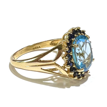 Yellow gold ring prong set with swiss blue topaz center stone and a halo of blue round blue sapphires.