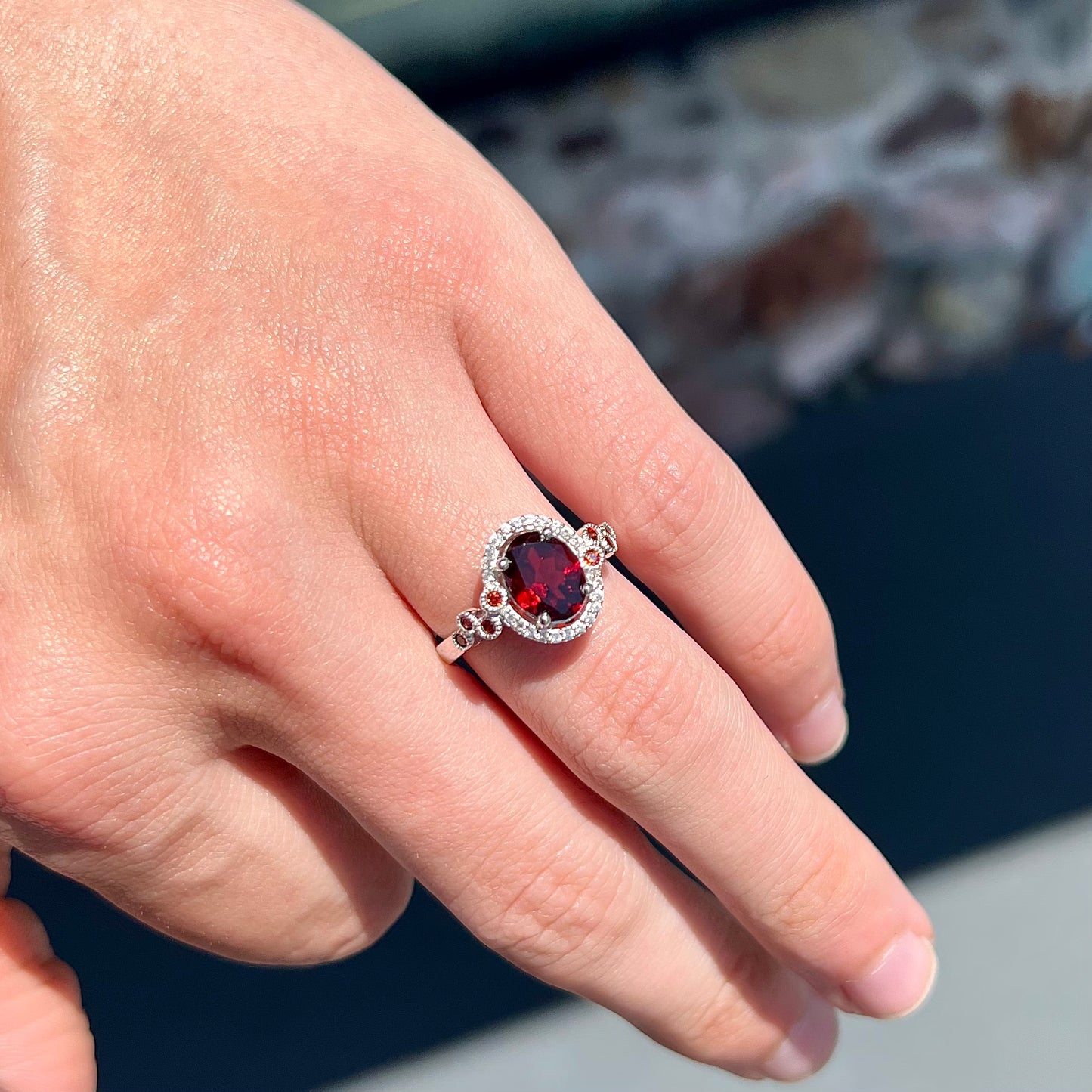A silver garnet and CZ halo ring.  The center stone is a red almandine garnet, and the side garnets are orange.