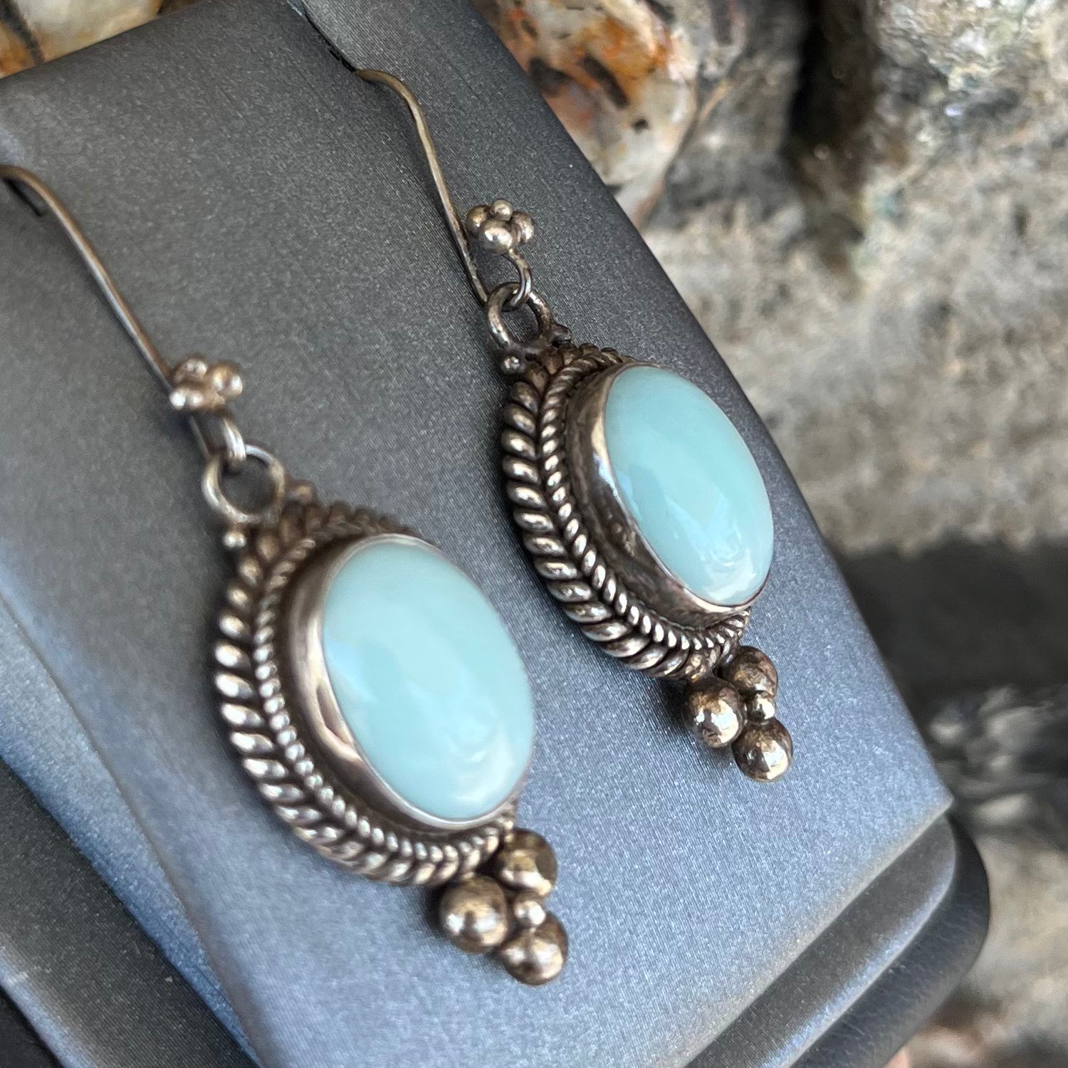 A pair of silver wire dangle earrings set with blue agate stones.  The earrings have a braided rope design.