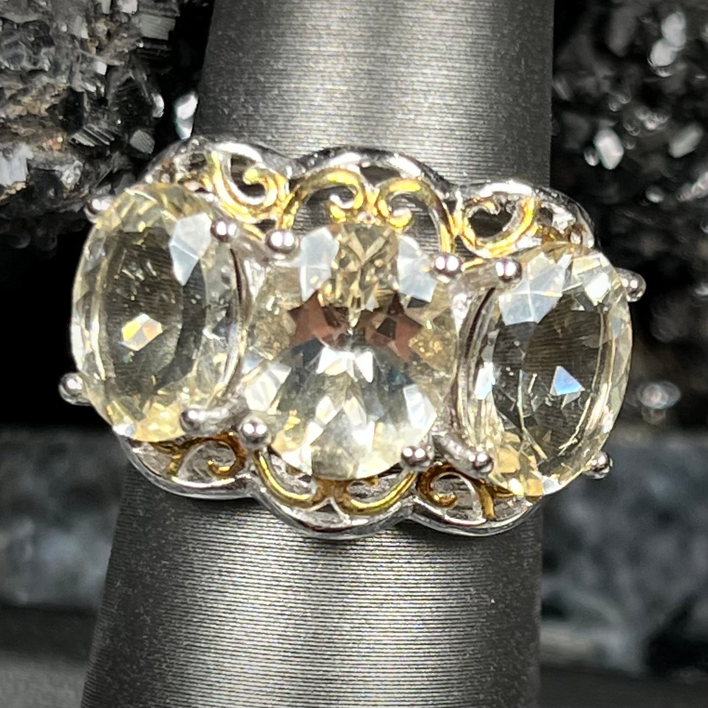 A sterling silver ring set with three oval cut golden beryl stones and yellow gold plated filigree accents.