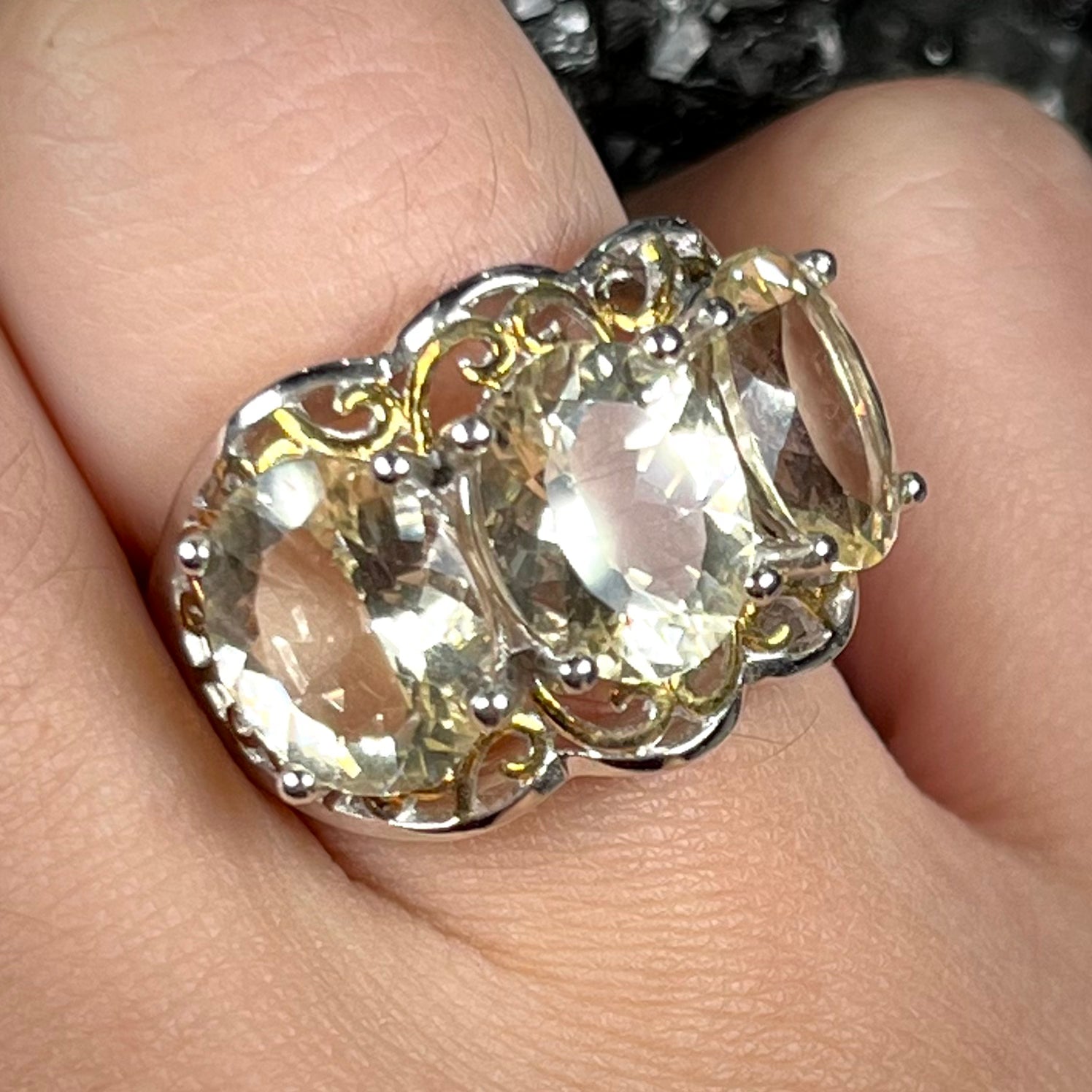 A sterling silver ring set with three oval cut golden beryl stones and yellow gold plated filigree accents.