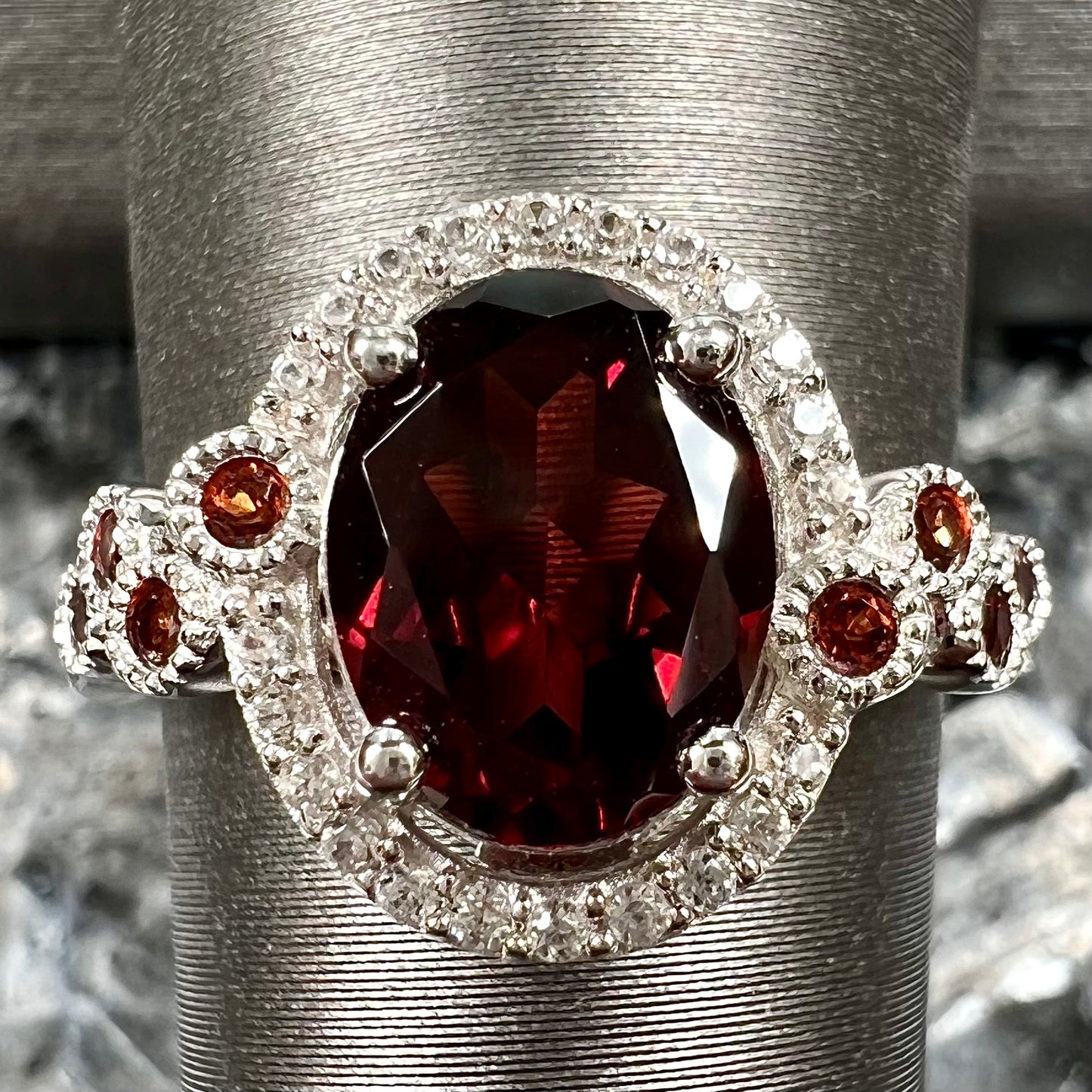 A silver garnet and CZ halo ring.  The center stone is a red almandine garnet, and the side garnets are orange.