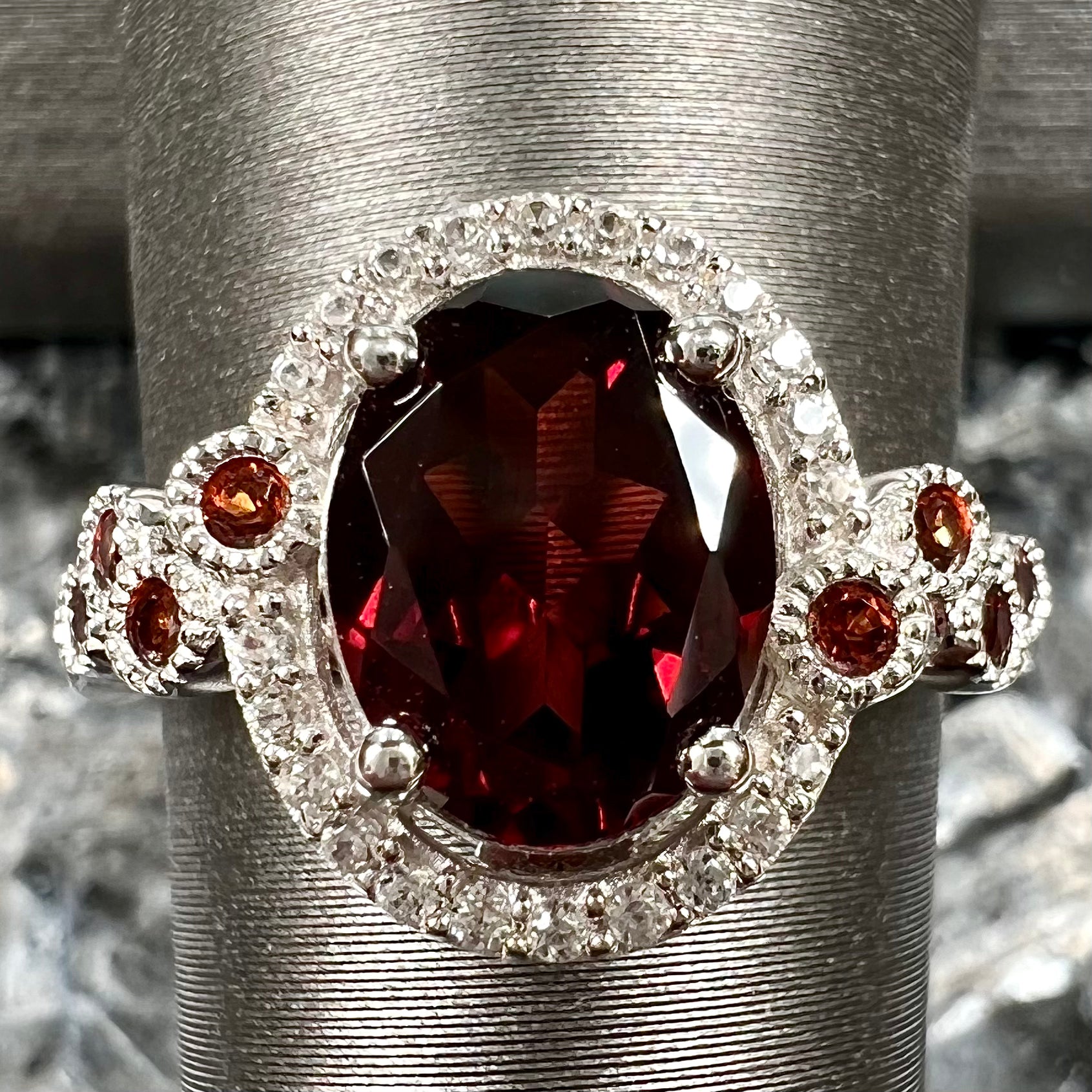 A silver garnet and CZ halo ring.  The center stone is a red almandine garnet, and the side garnets are orange.