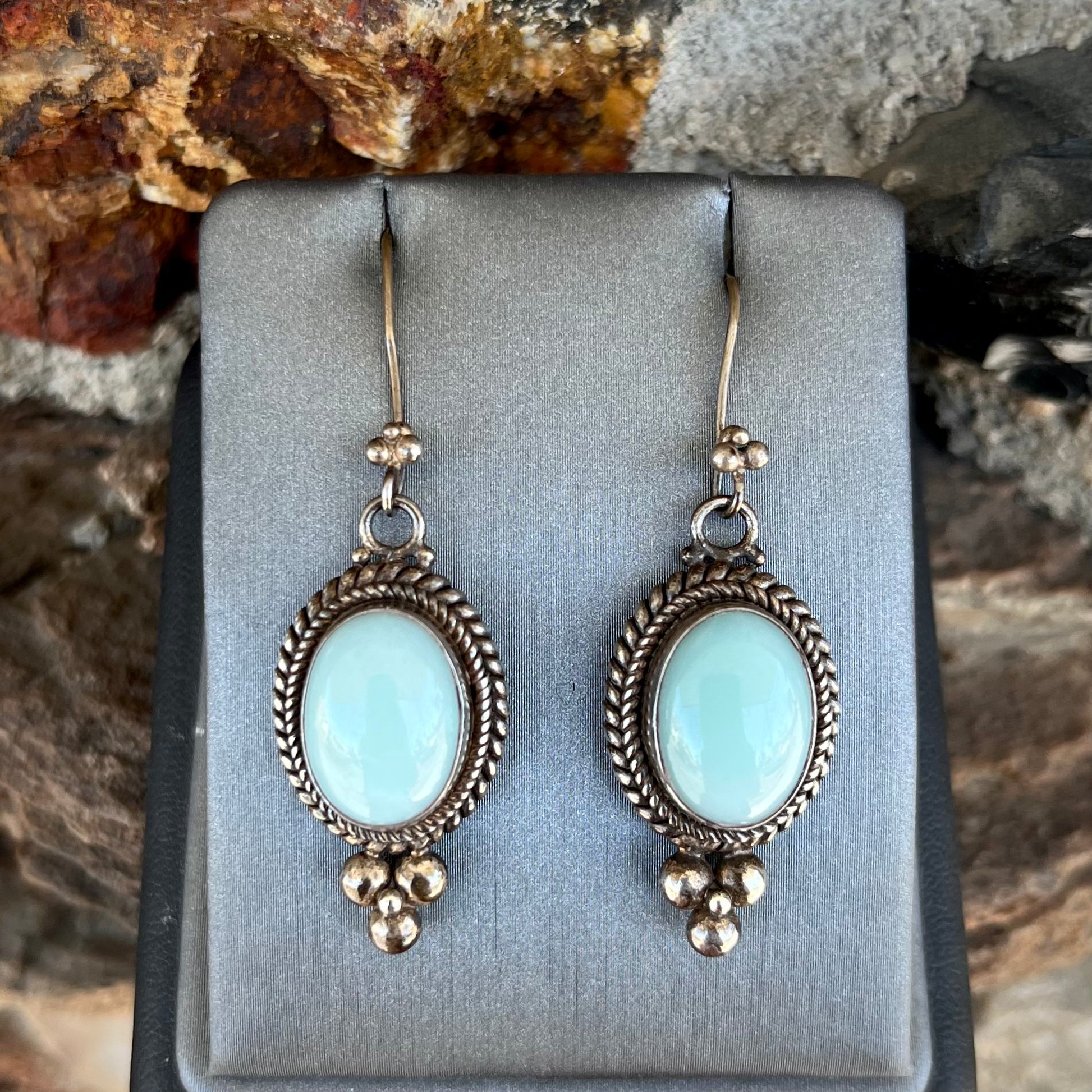 A pair of silver wire dangle earrings set with blue agate stones.  The earrings have a braided rope design.