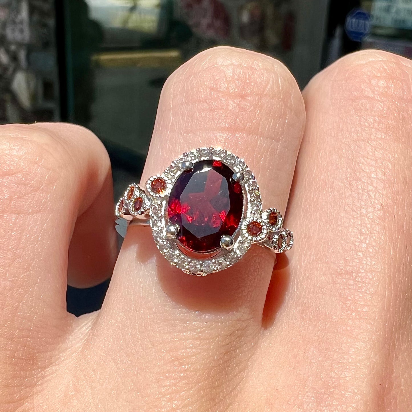 A silver garnet and CZ halo ring.  The center stone is a red almandine garnet, and the side garnets are orange.