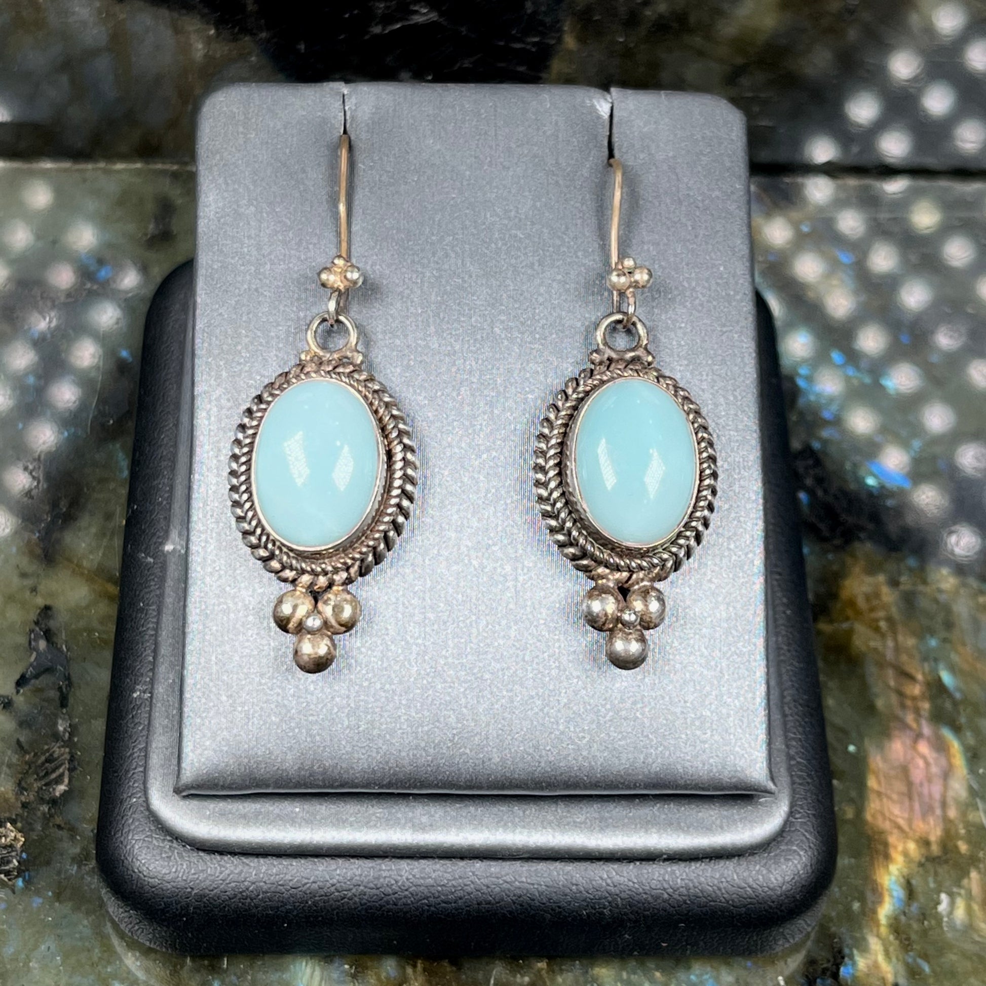A pair of silver wire dangle earrings set with blue agate stones.  The earrings have a braided rope design.