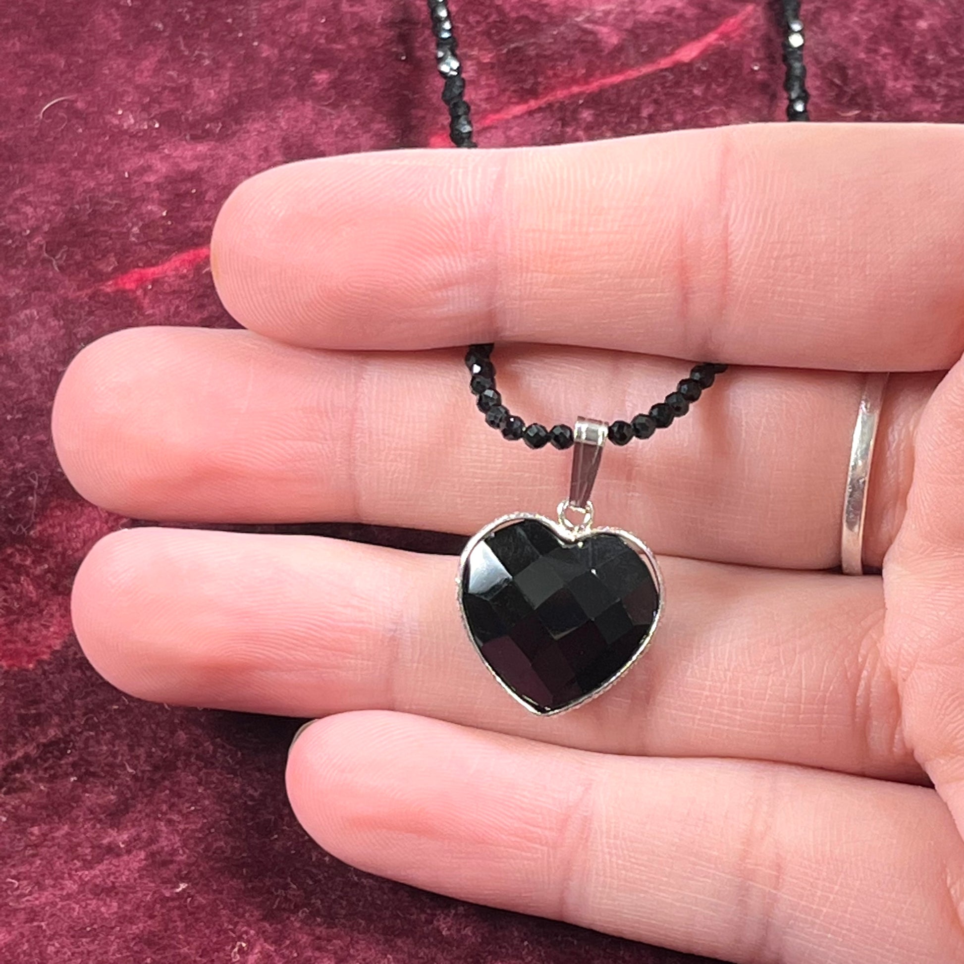 A silver heart shape black stone necklace.  The heart is a faceted cut black spinel, and the pendant is on faceted black spinel beads.