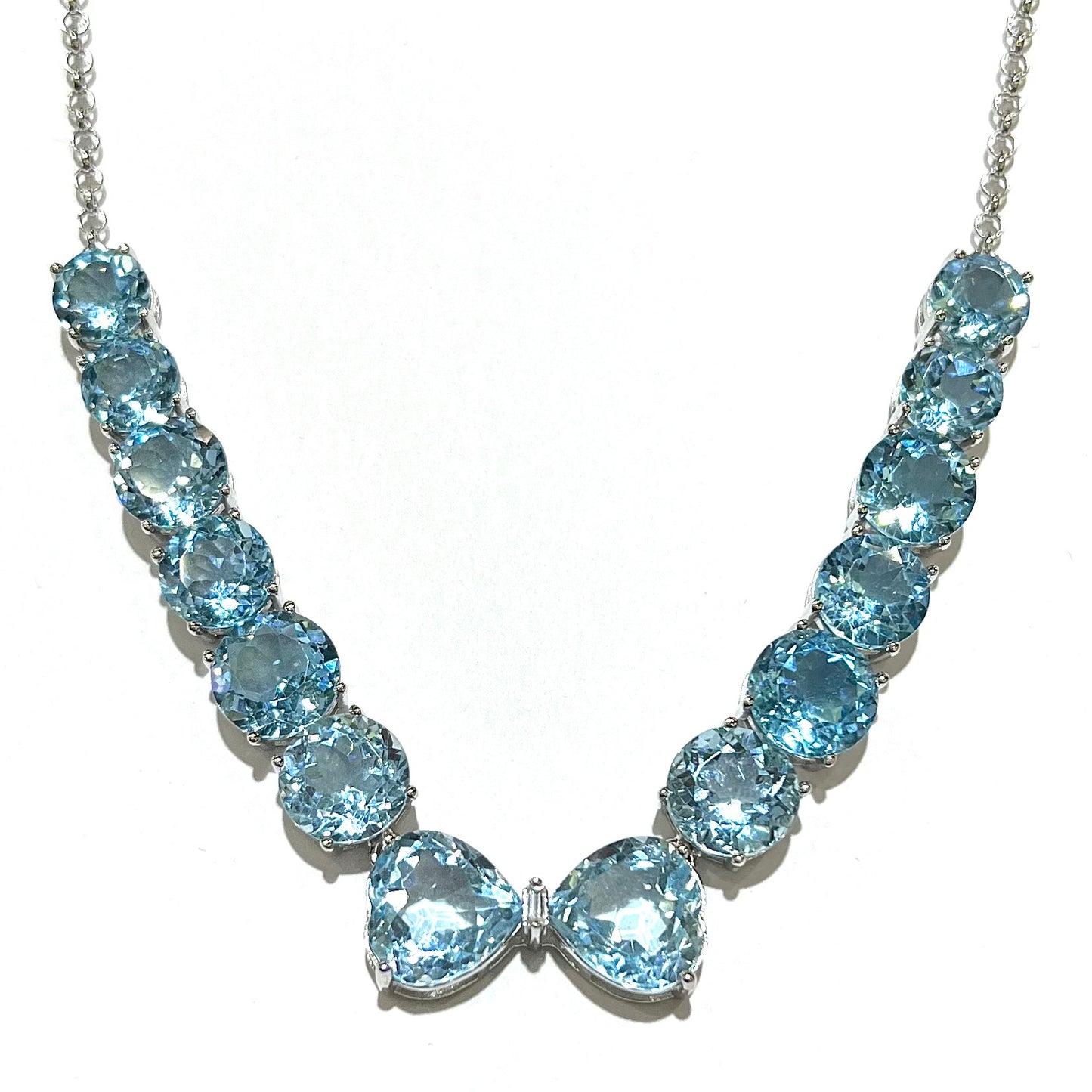 A string of twelve round brilliant cut sky-blue topaz gemstones with two heart shaped topaz gems and a single emerald cut white zircon between them on a sterling silver chain.