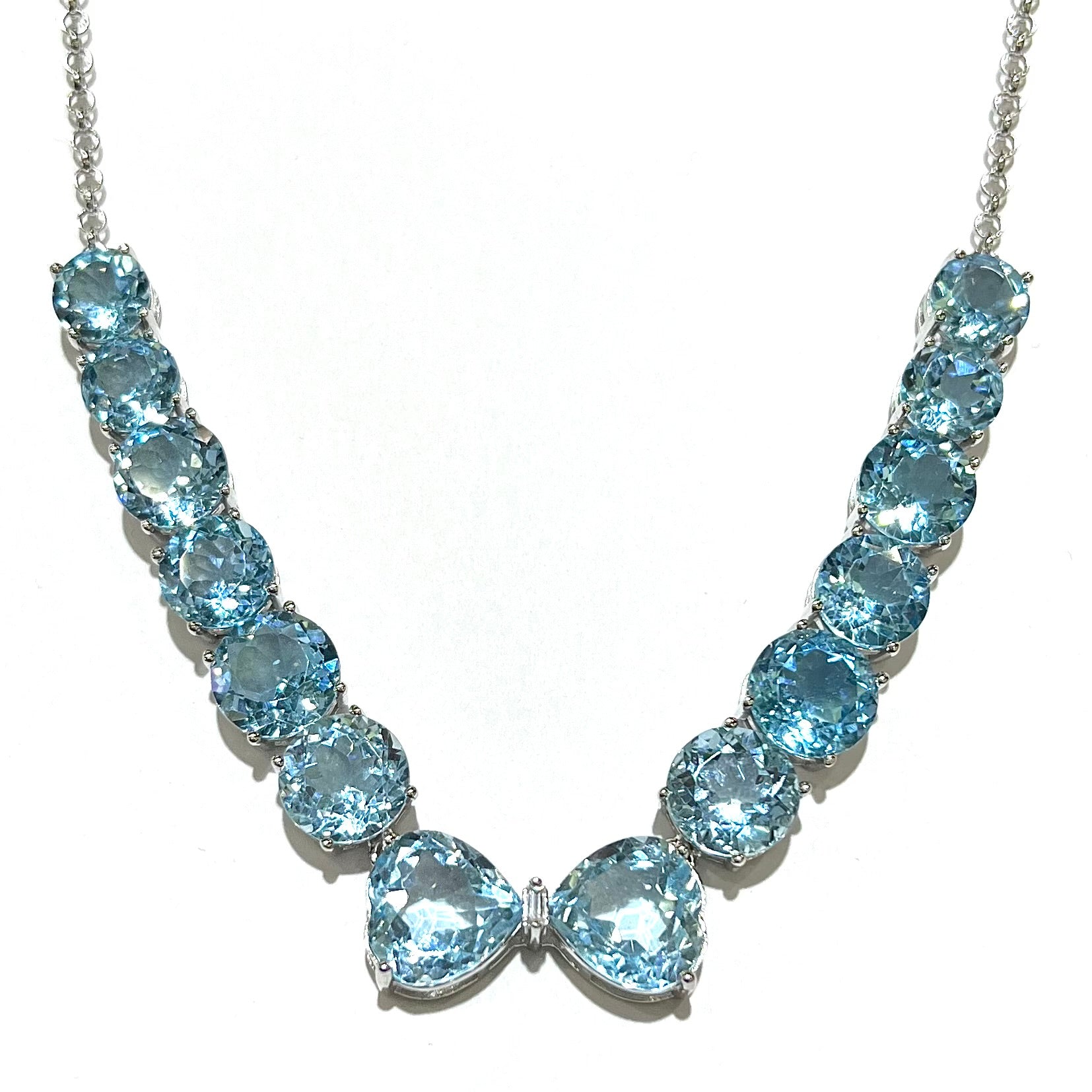 A string of twelve round brilliant cut sky-blue topaz gemstones with two heart shaped topaz gems and a single emerald cut white zircon between them on a sterling silver chain.