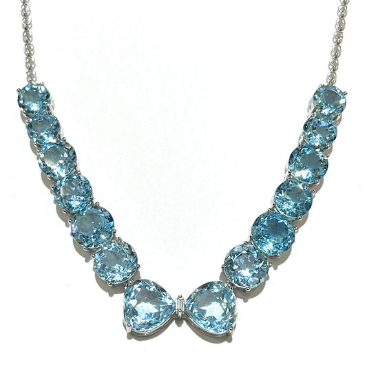 A string of twelve round brilliant cut sky-blue topaz gemstones with two heart shaped topaz gems and a single emerald cut white zircon between them on a sterling silver chain.