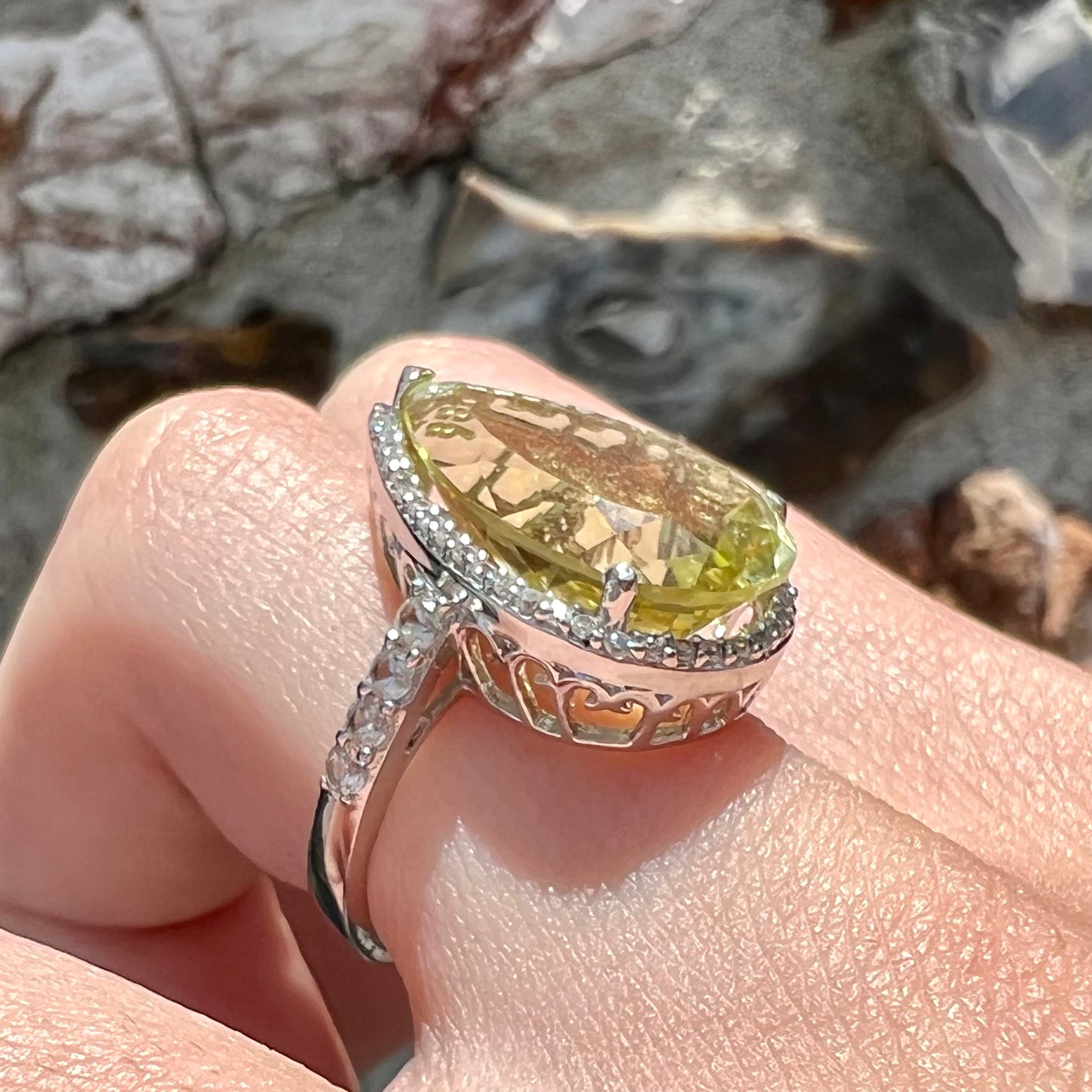 A pear shape lemon quartz set in a sterling silver and white topaz halo ring.