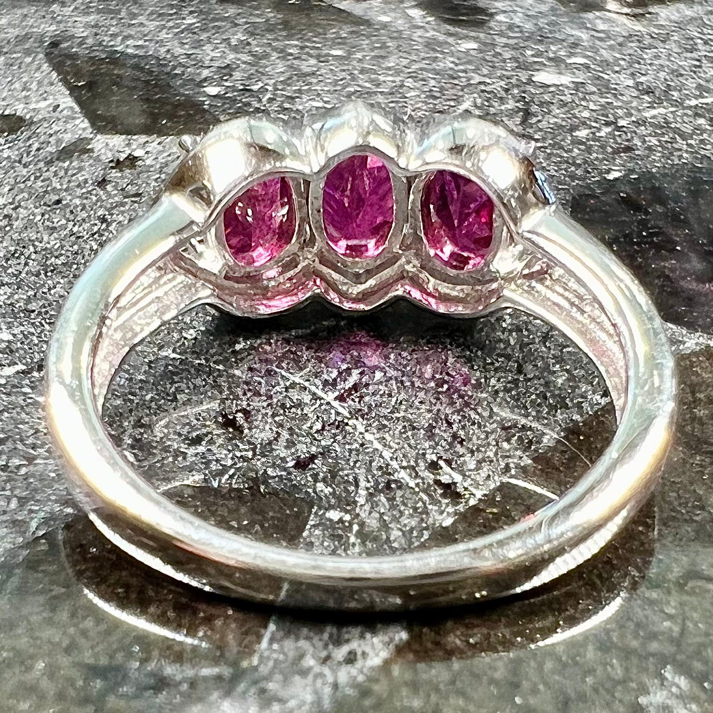 A three stone past, present, and future purple faceted oval cut rhodolite garnet ring.