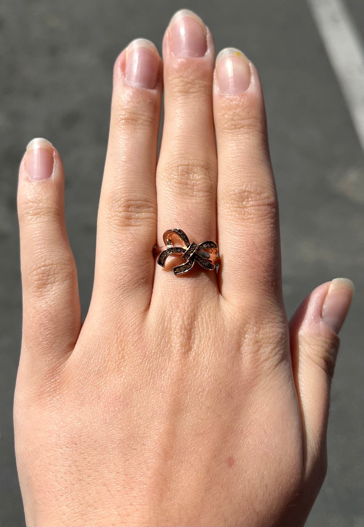 A rose gold colored bow ring.  The bow is tied in a knot, and the knot is set with cognac cubic zirconia.