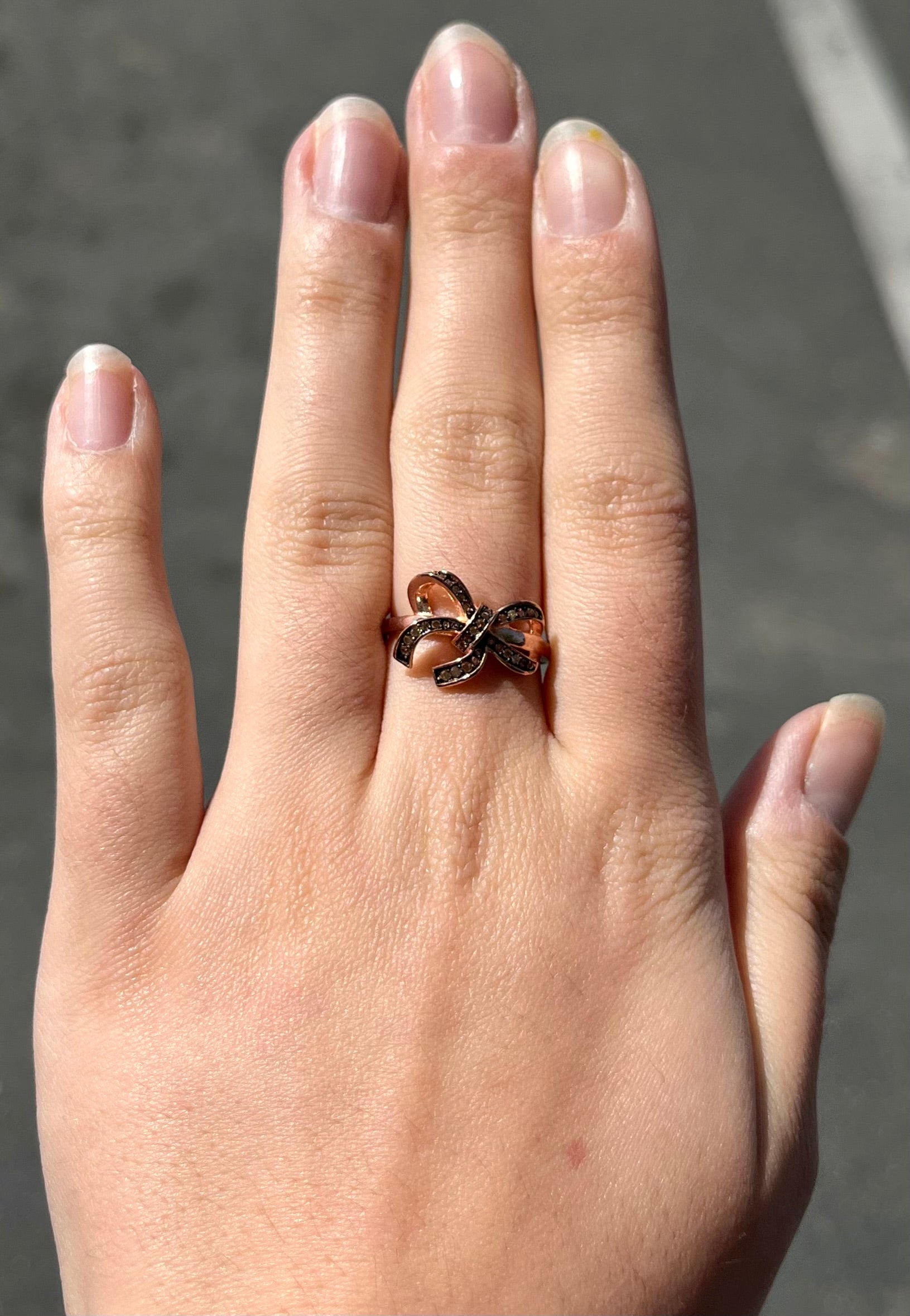 A rose gold colored bow ring.  The bow is tied in a knot, and the knot is set with cognac cubic zirconia.