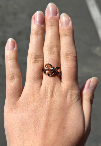 A rose gold colored bow ring.  The bow is tied in a knot, and the knot is set with cognac cubic zirconia.