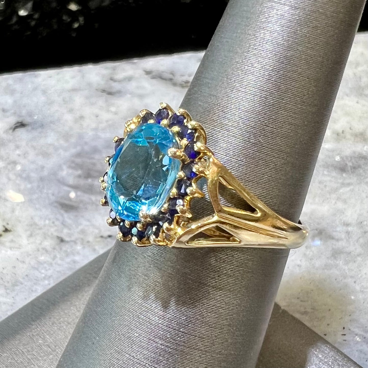 Yellow gold ring prong set with swiss blue topaz center stone and a halo of blue round blue sapphires.