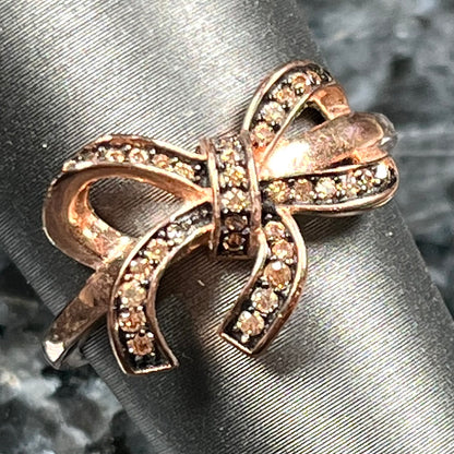 A rose gold colored bow ring.  The bow is tied in a knot, and the knot is set with cognac cubic zirconia.