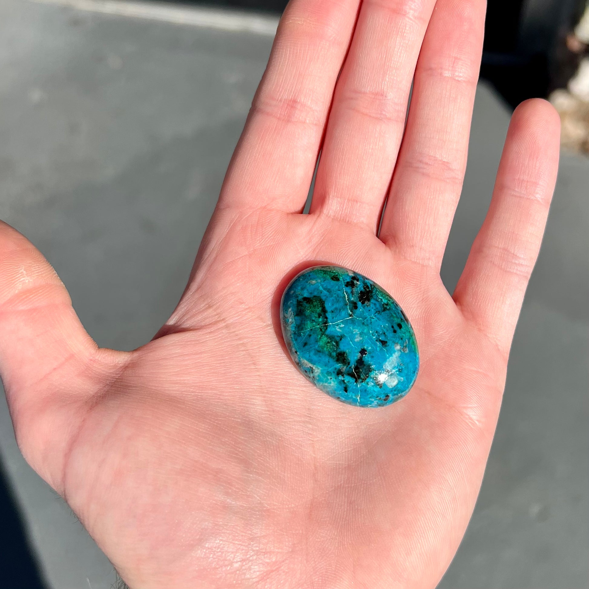 An oval cabochon cut blue chrysocolla with green malachite inclusions.