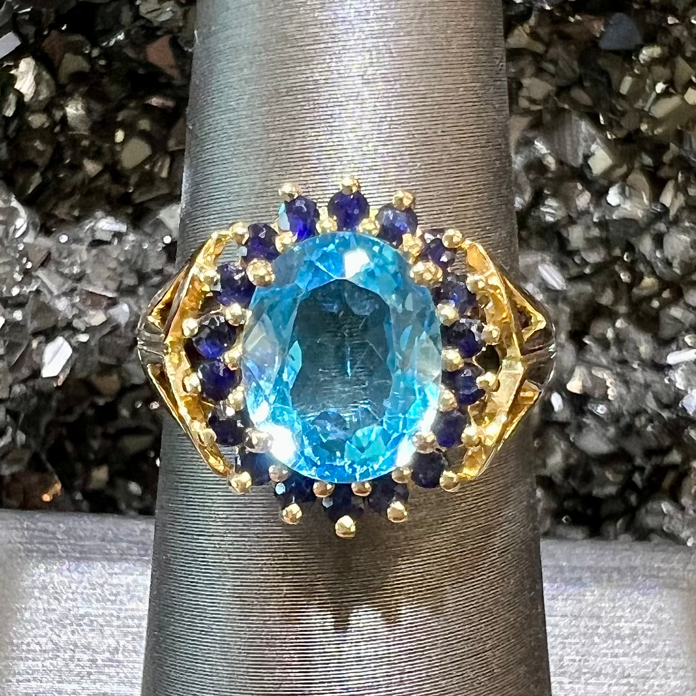 Yellow gold ring prong set with swiss blue topaz center stone and a halo of blue round blue sapphires.